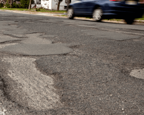 A damaged asphalt street with lots of potholes.